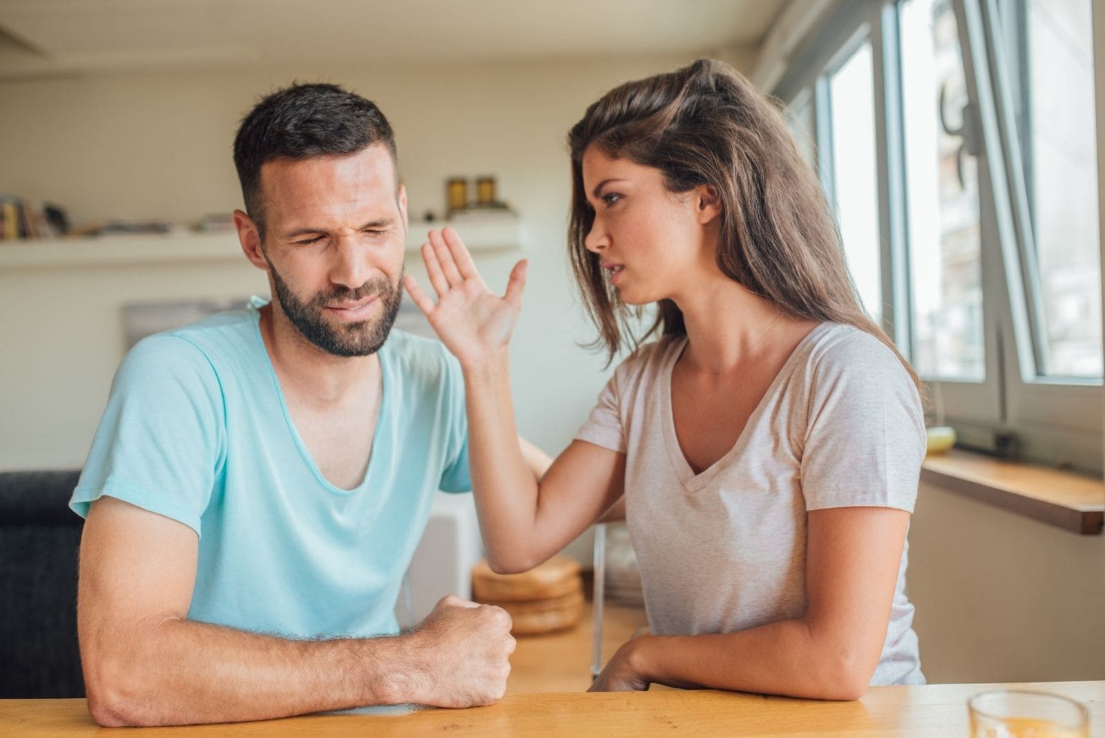 young woman is hitting her husband while sitting in the dining room