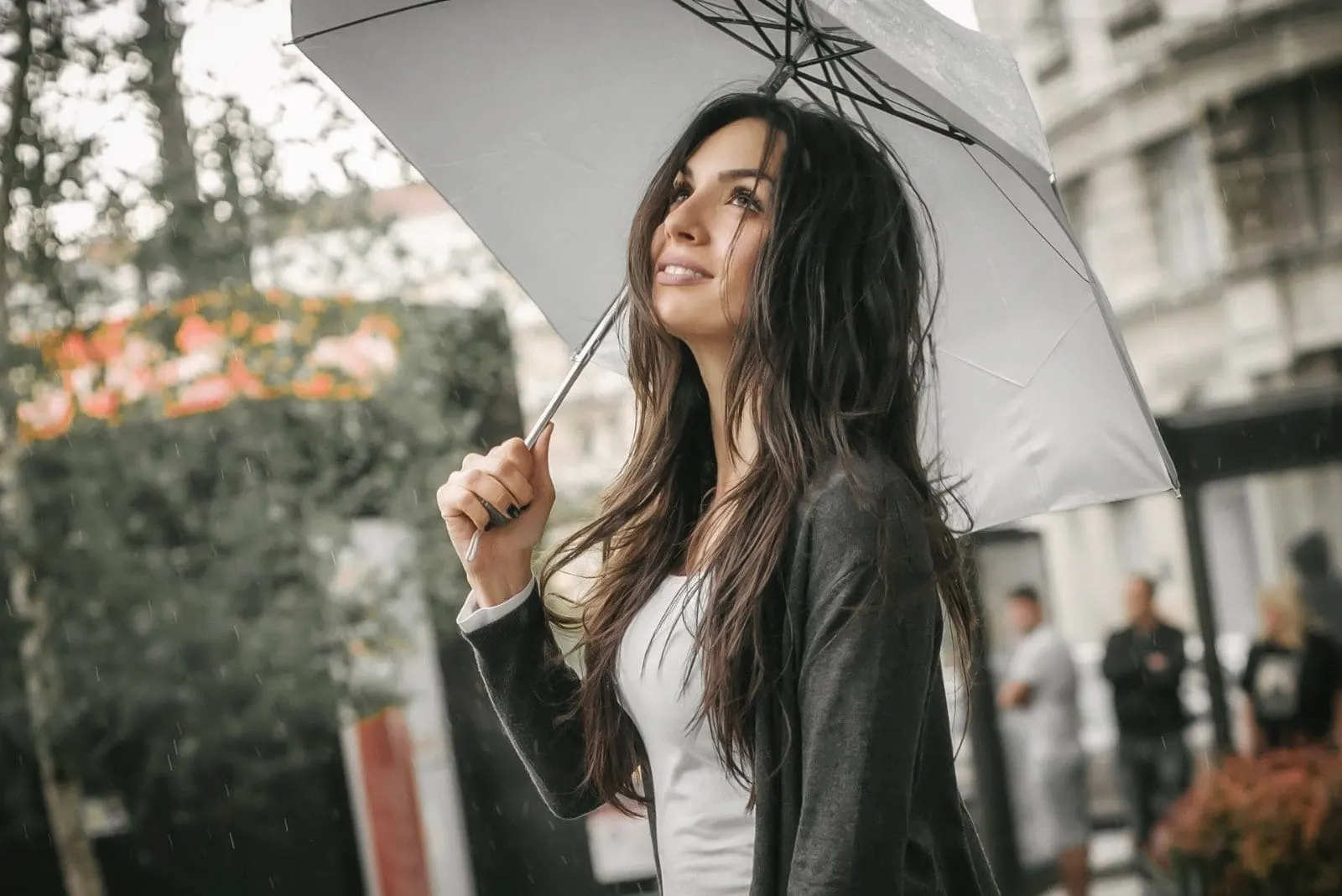 young woman smiling even its raining and bringing an umbrella outdoors