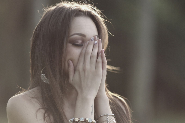 donna triste in procinto di piangere che si copre parzialmente il viso con le mani indossando gioielli e chiudendo gli occhi