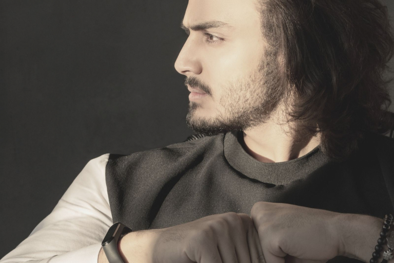 jovem bonito com cabelo comprido, pensativo e a olhar para a sua direita enquanto está sentado