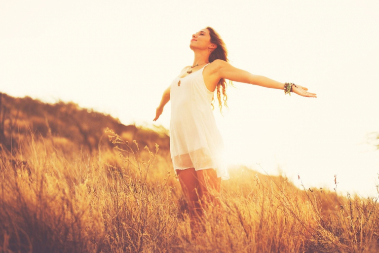 happy young woman in fashion standing and spreading arms in the middle of the field during sunset