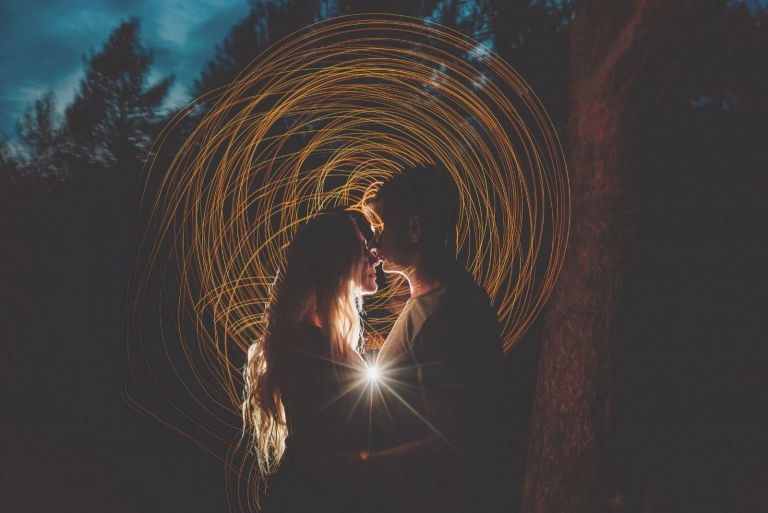 casal a beijar-se no escuro com uma longa faixa de luz a rodear o casal