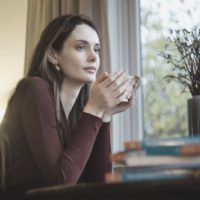 pensive woman having coffee in the morning inside the house sitting near the windows