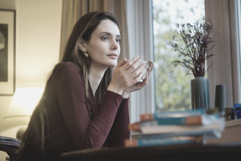 pensive woman having coffee in the morning inside the house sitting near the windows