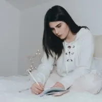 woman writing on notebook while sitting on bed