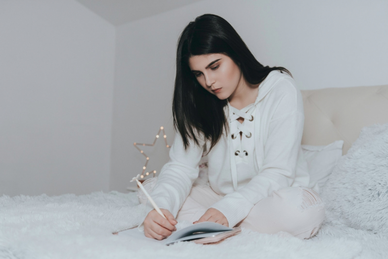 woman writing on notebook while sitting on bed
