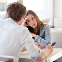 mujer enfadada escuchando hablar al hombre sentado junto a la mesa en el interior de una cafetería