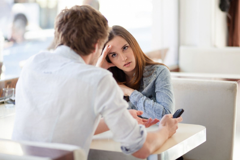 angry woman listening to the man talking while sitting by the table inside a cafe