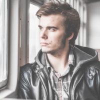 young pensive man sitting on the train near the window looking outside