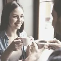 woman and man drinking coffee inside a cafe smiling and talking
