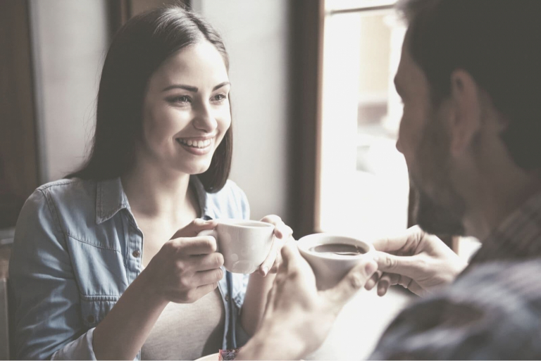woman and man drinking coffee inside a cafe smiling and talking