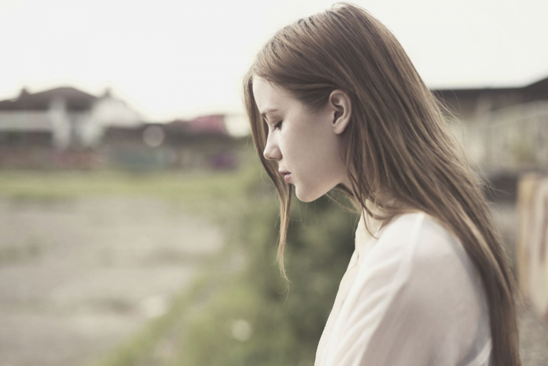 pensive woman sitting outdoors with head down in the daytime