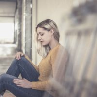 young woman sitting on the floor of the hallway of a building thoughtful and sad