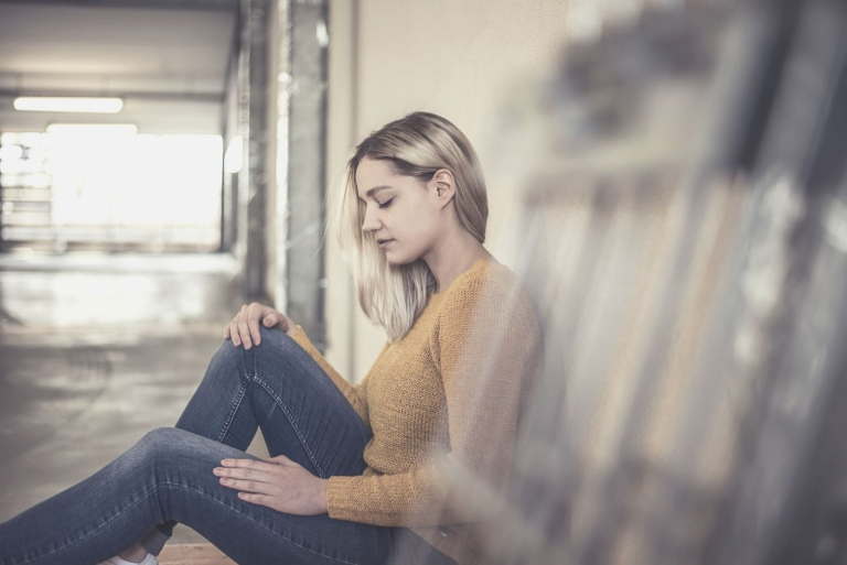 young woman sitting on the floor of the hallway of a building thoughtful and sad