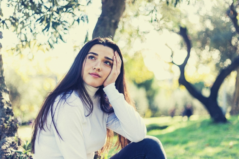 pretty woman thinking deeply sitting on the ground of the forest park