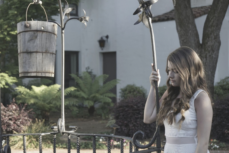pretty young woman standing on the park holding on the fence wearing white dress