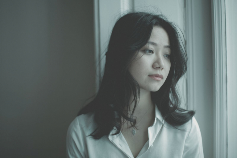 sad pensive woman looking outside thru the window wearing white top