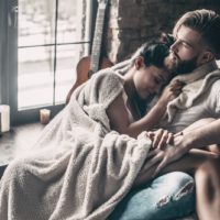 beautiful young couple covered with blanket resting together while sitting on an armchair