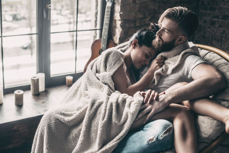 beautiful young couple covered with blanket resting together while sitting on an armchair