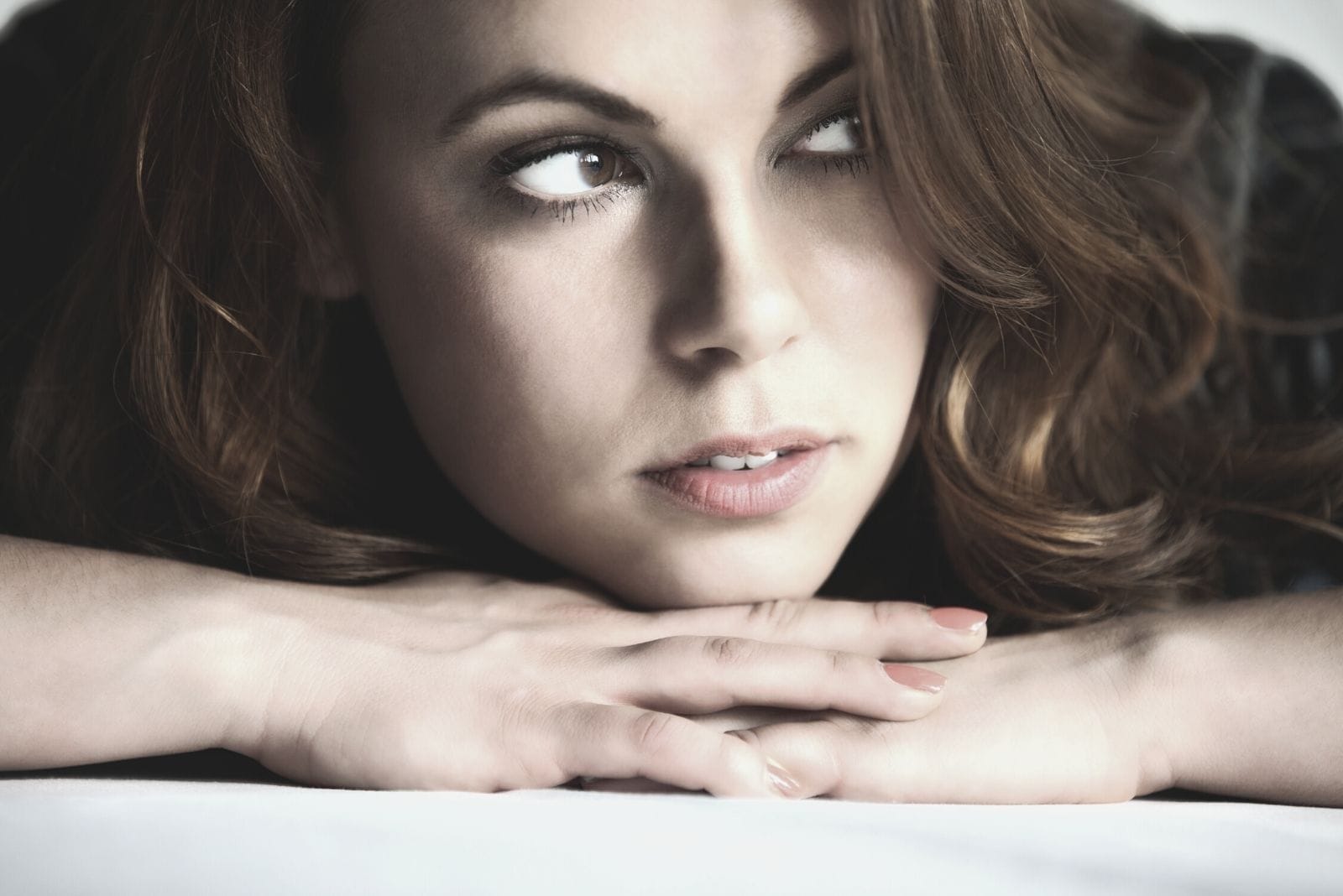 portrait of a young pensive woman in close photography and looking to the side with head leaning over her hands on the table
