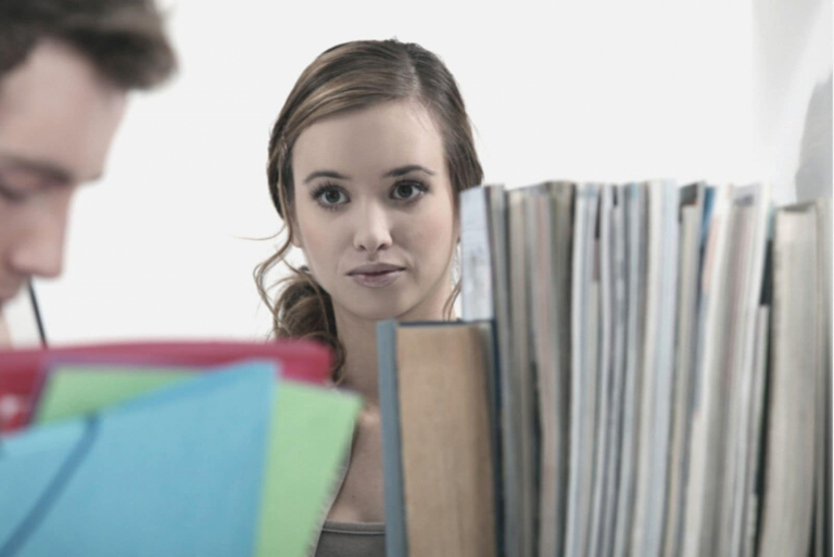 young pretty woman looking at a man from a far filing magazines/books inside library