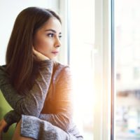 pensive woman looking through window while sitting indoor