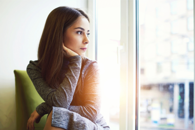 pensive woman looking through window while sitting indoor