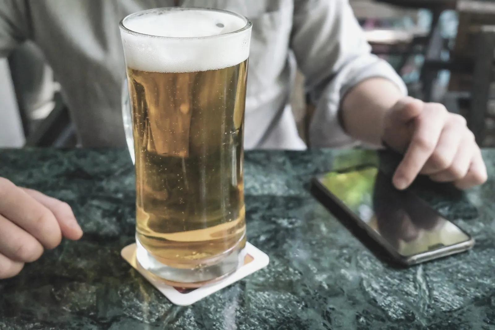 a glass of beer placed on the table with a cropped image of a woman pressing on the keys of the smartphone on the table