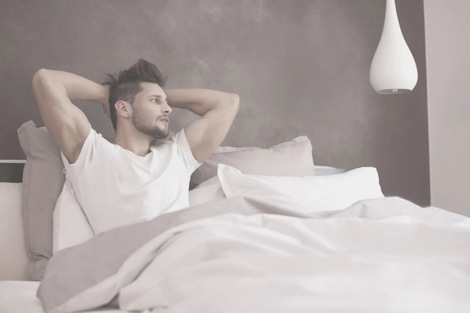 a handsome man in bed thinking deeply placing his hands at the back of his head
