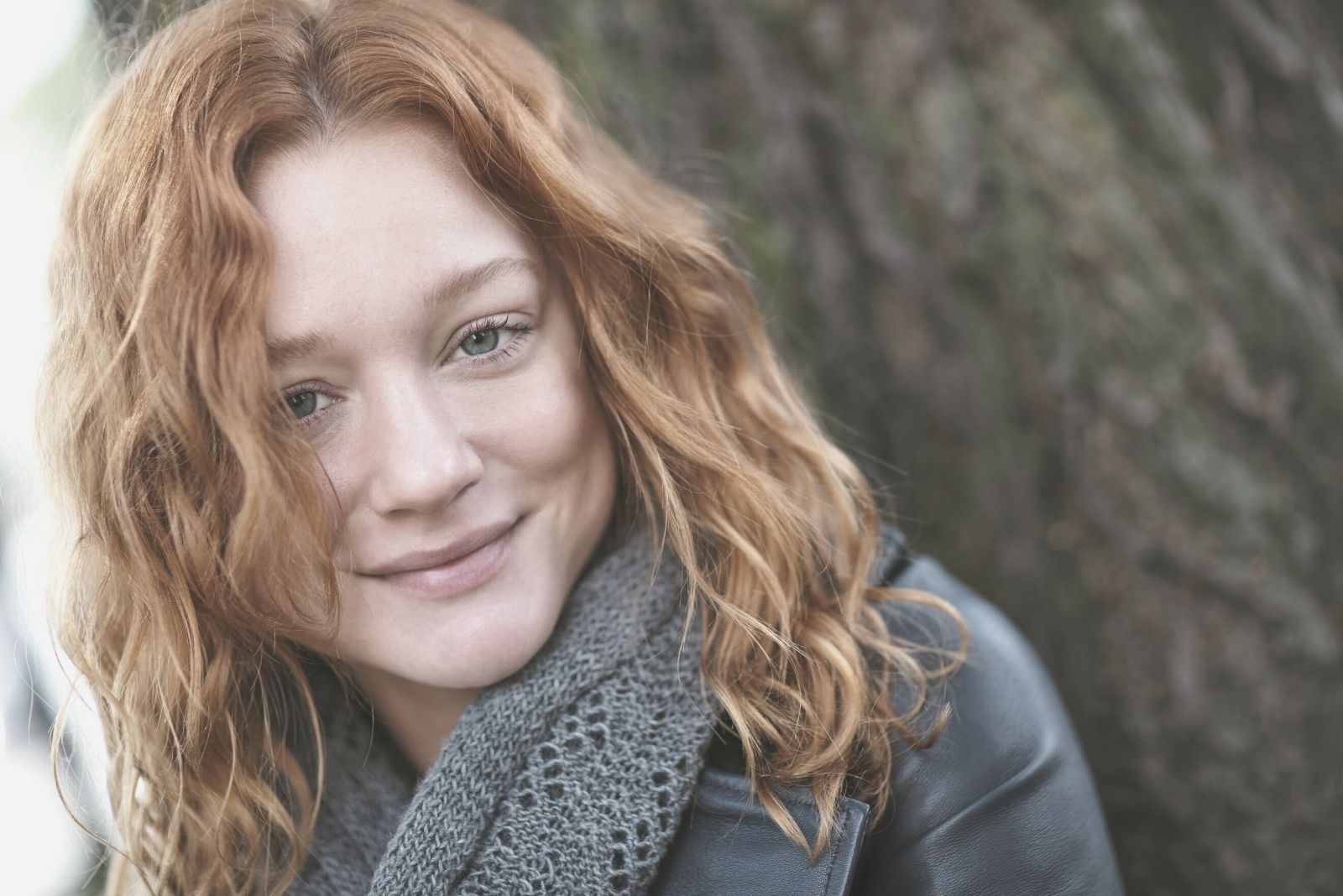 uma jovem mulher a sorrir ao ar livre num parque junto a uma árvore