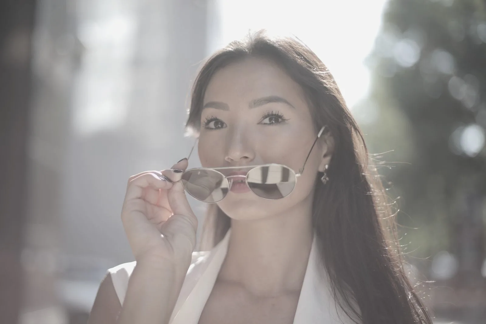 asian woman in white top holding a sunglass while walking outdoors