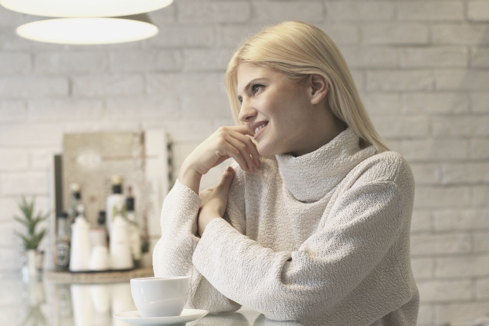 hermosa mujer rubia sonriendo por la mañana sentado en la encimera de la cocina sonriendo