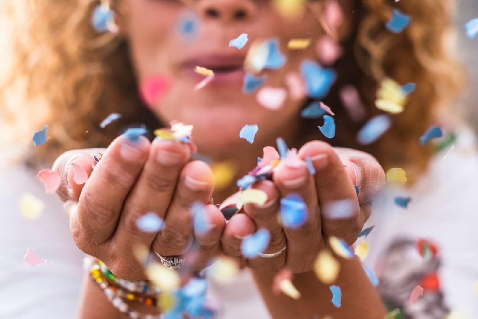 beautiful defocused woman blowing confetti on hand for celebration concept