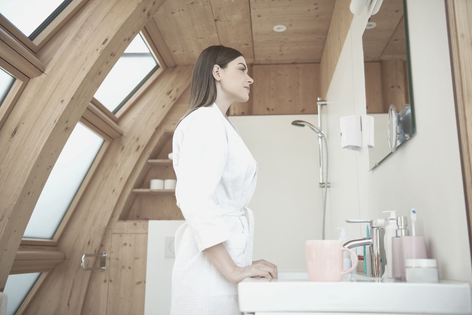 bella donna che sorride e guarda lo specchio all'interno del bagno indossando un accappatoio in vista laterale angolo basso