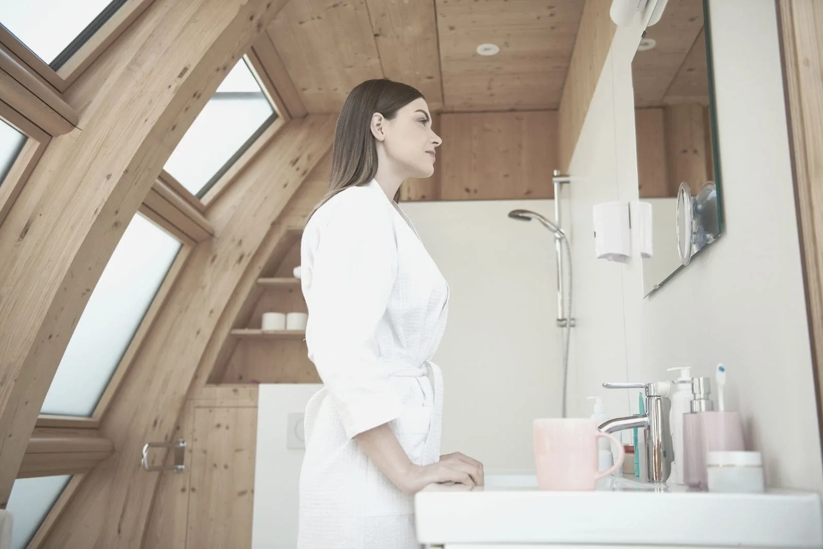 beautiful woman smiling and looking at the mirro inside the bathroom wearing a robe in sideview low angle
