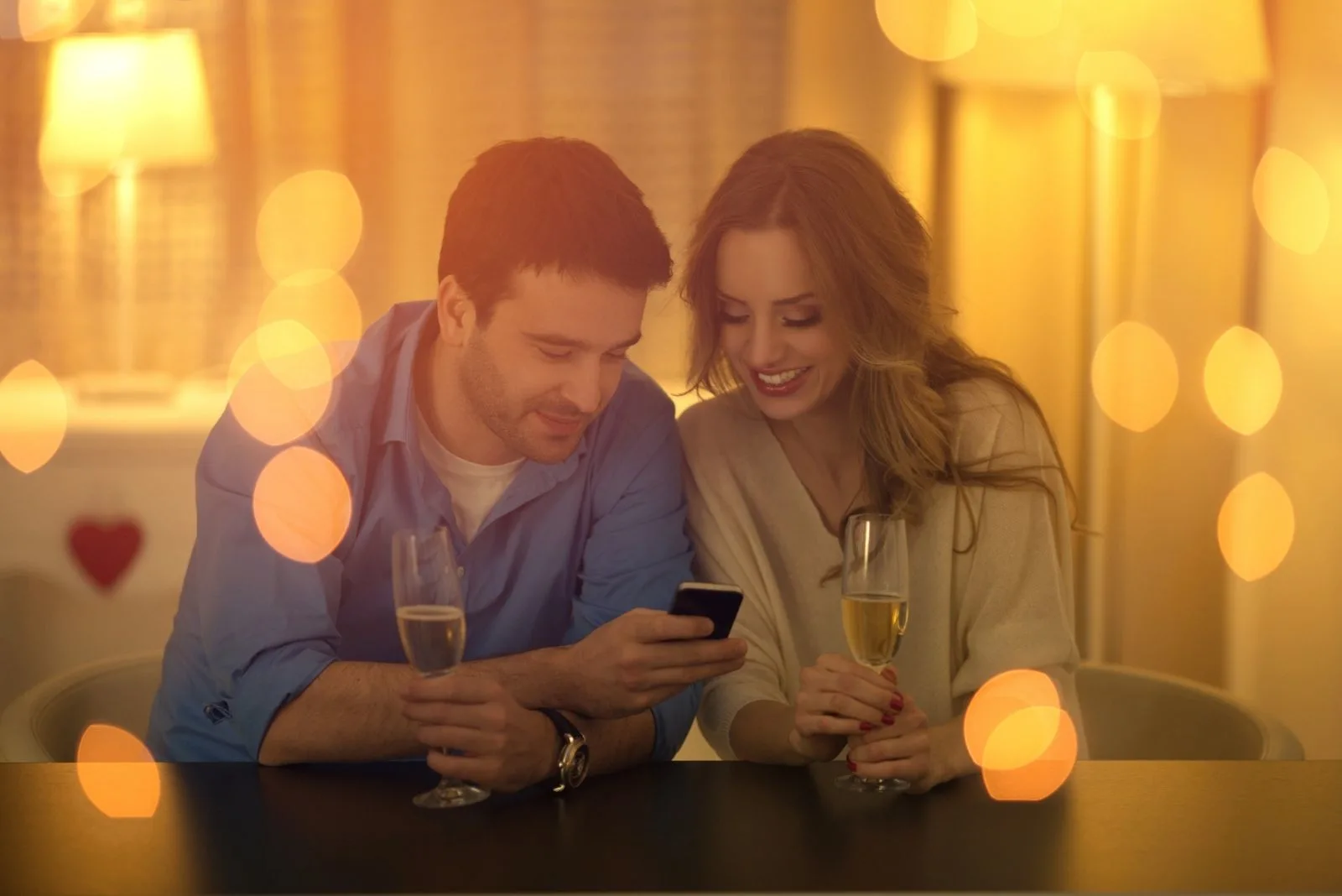beautiful young couple looking at the smartphone during a date with lights in photographic effect
