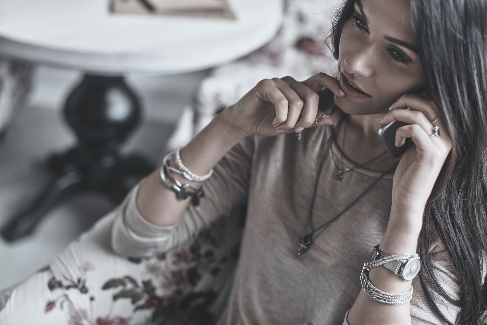 hermosa mujer joven tocando su barbilla mientras habla por el teléfono sentado en un sofá en el interior