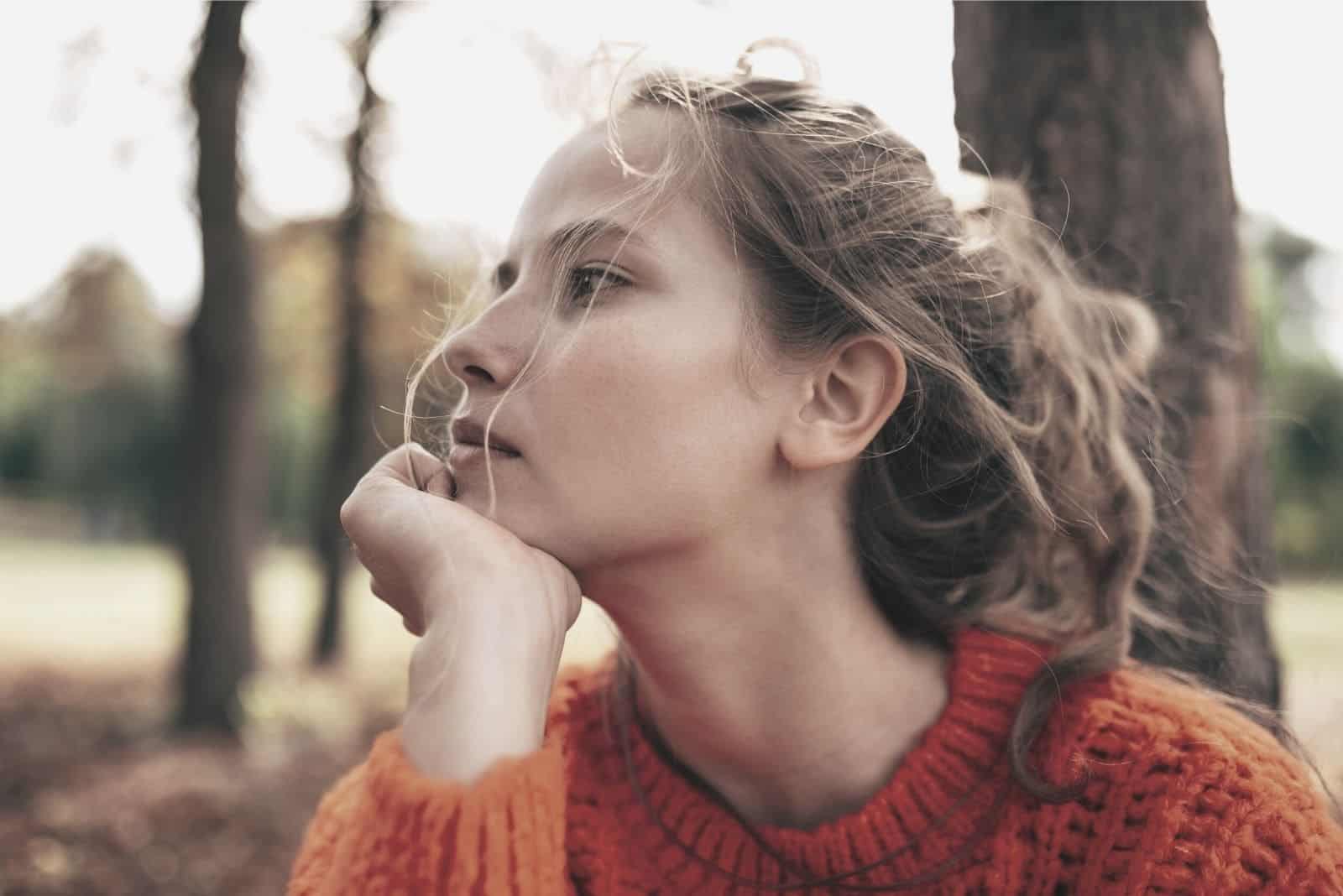 blonde curly haired woman thinking deeply with head leaning on her hand sitting outdoors