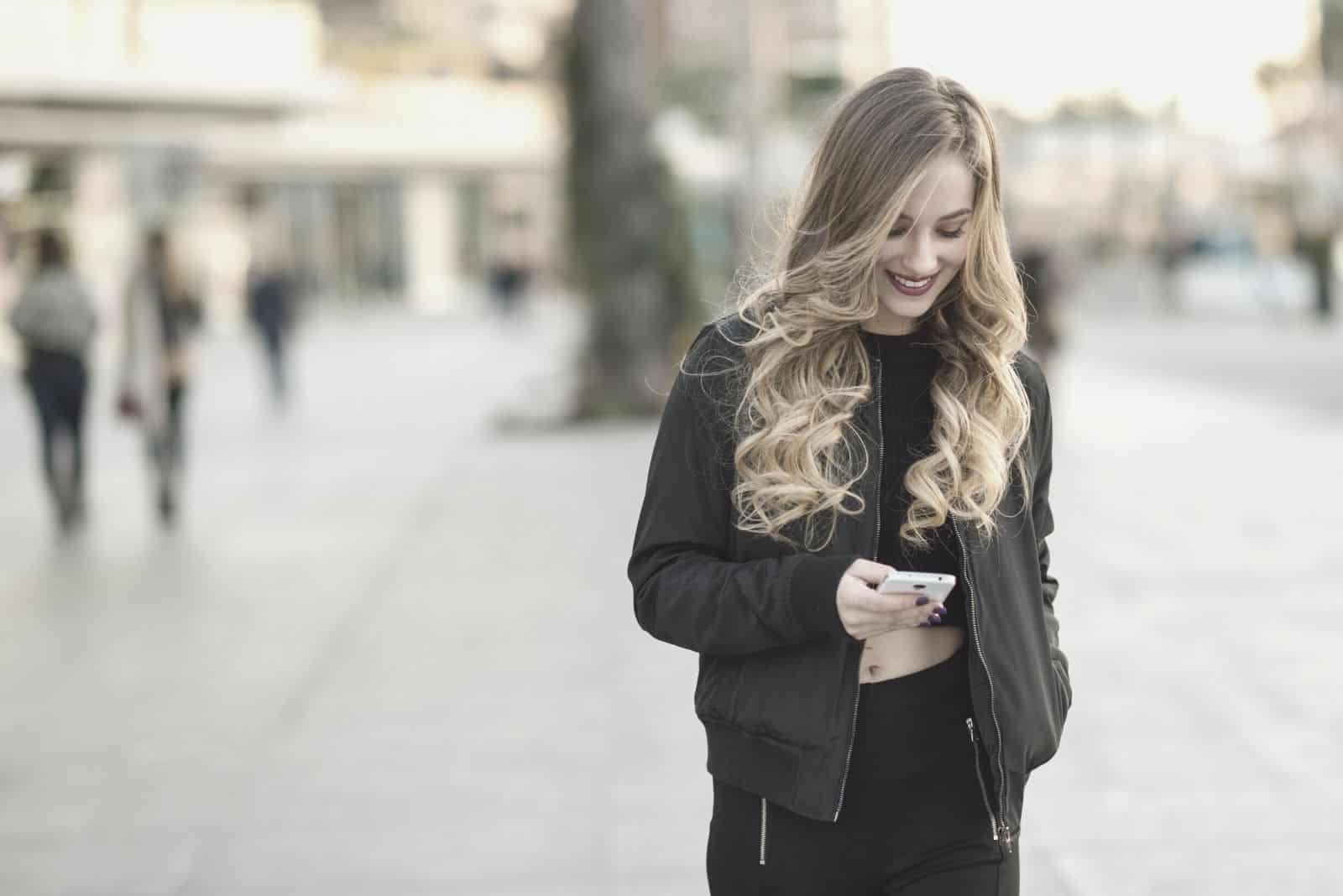 blonde woman texting in the street black cropped top