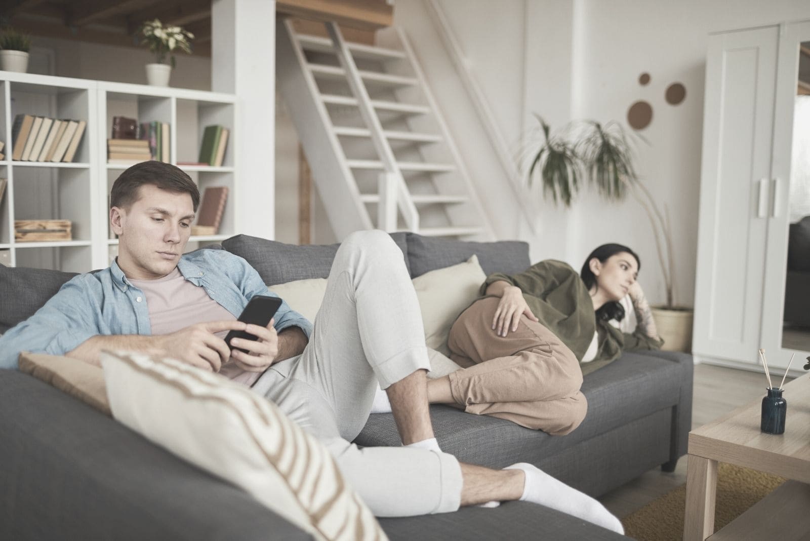 Coppia annoiata a casa che guarda la tv sul divano con l'attenzione sull'uomo impegnato con il suo gadget