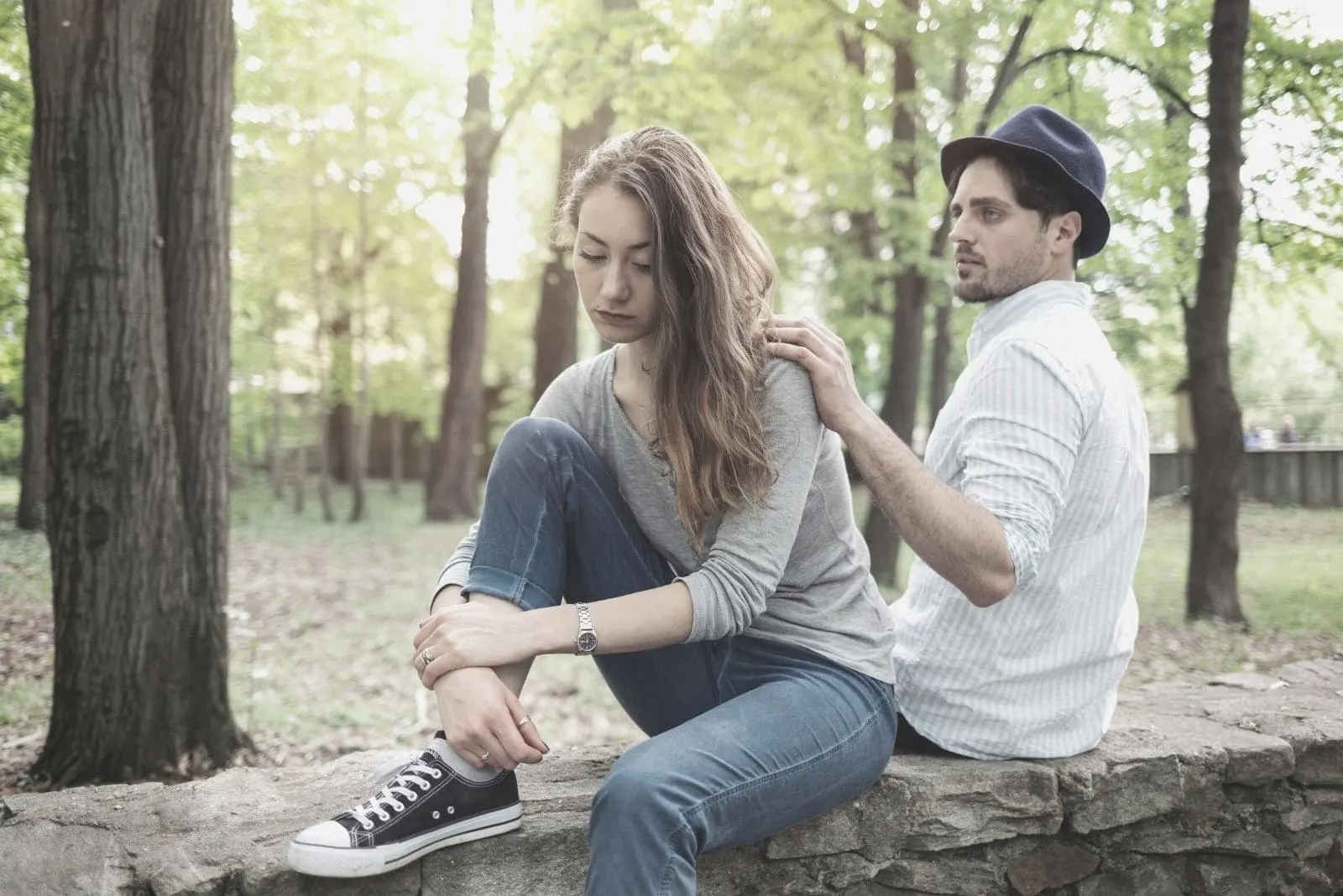 boyfriend looking worried tapping woman's shoulder breaking up while sitting in the bench in the park