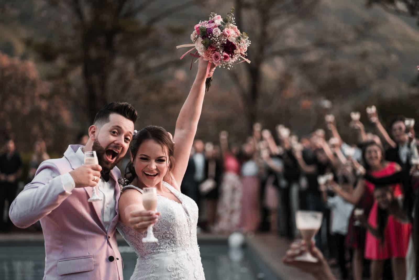 bride and groom holding wine glasses while standing near pool