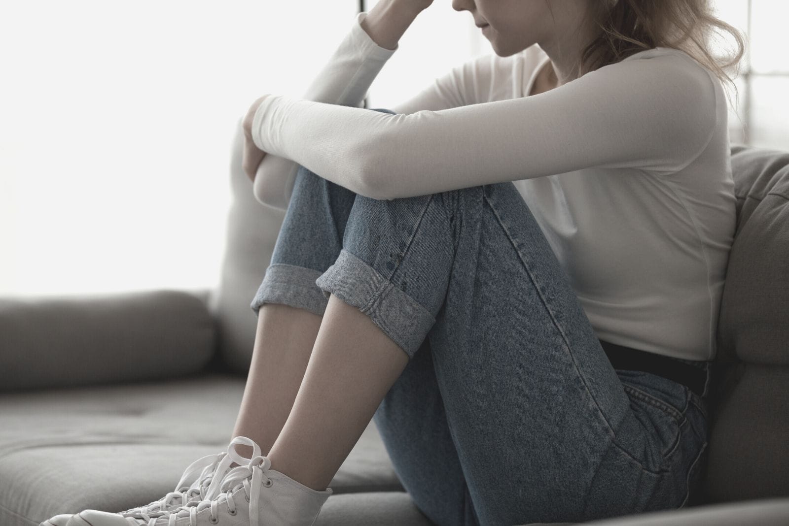 close up image of an upset woman sitting on the sofa with feet tucked in cropped image