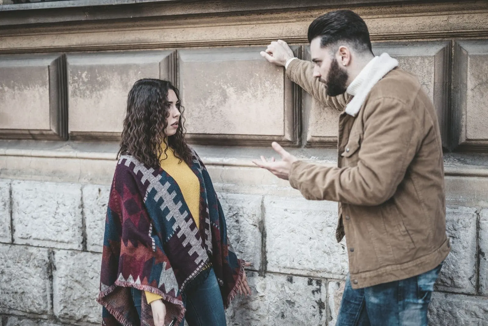couple arguing outdoors near a large brick wall in the street