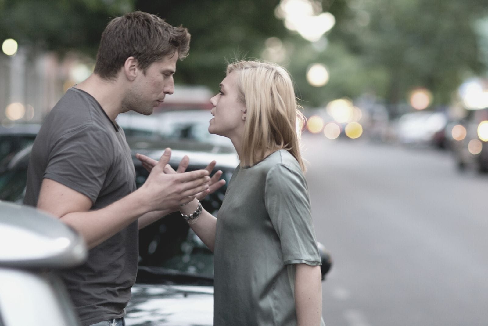 coppia che discute all'aperto in piedi vicino alle auto parcheggiate vicino alla strada