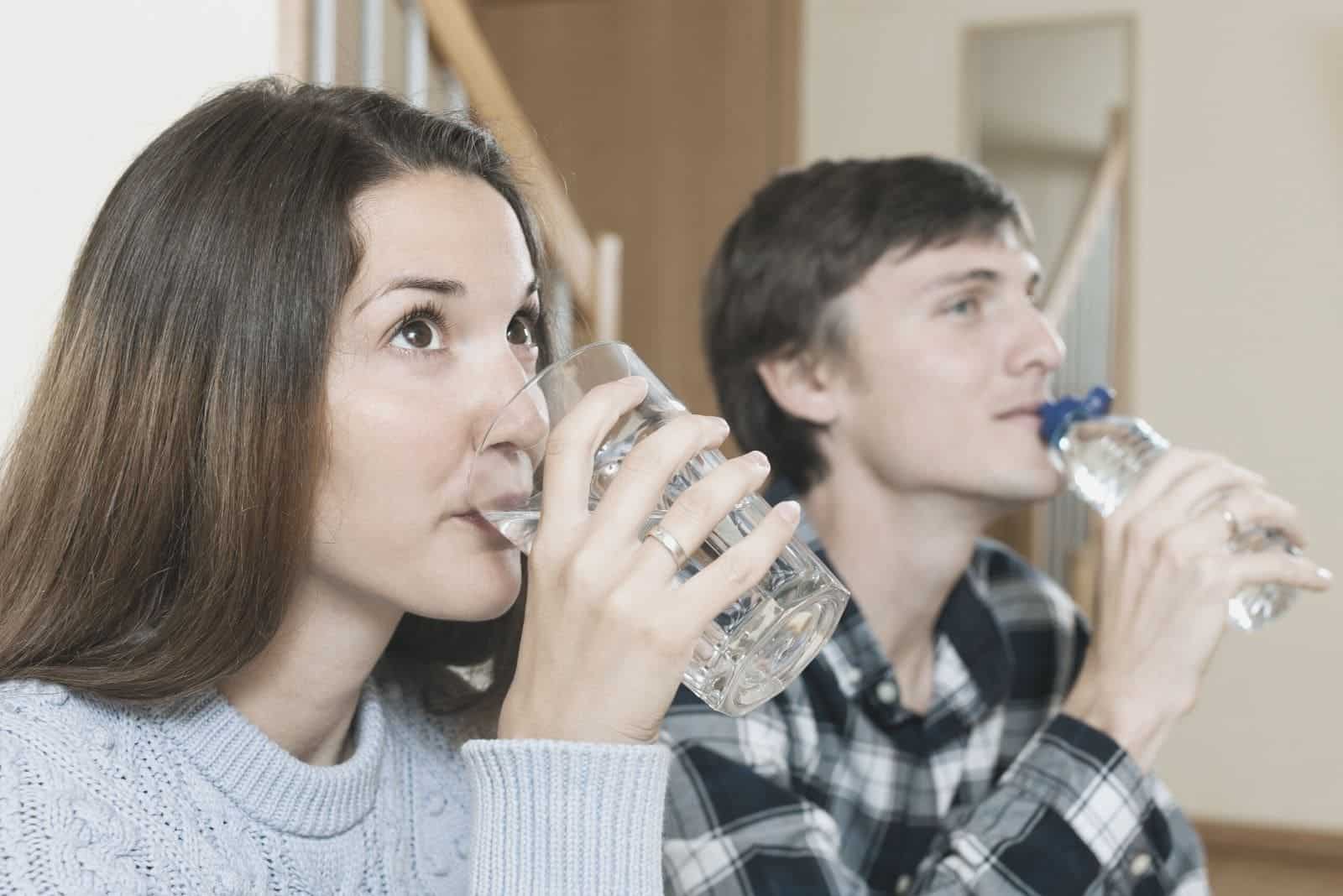 coppia che beve acqua contemporaneamente mentre è seduta in casa
