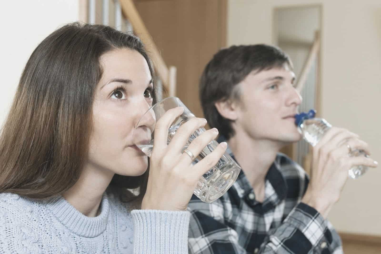 couple drinking water at the same time while sitting in home