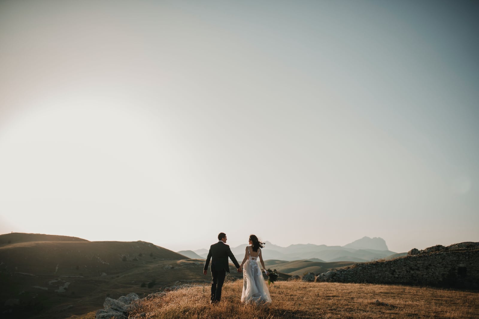 groom and bride holding hands while standing in the field