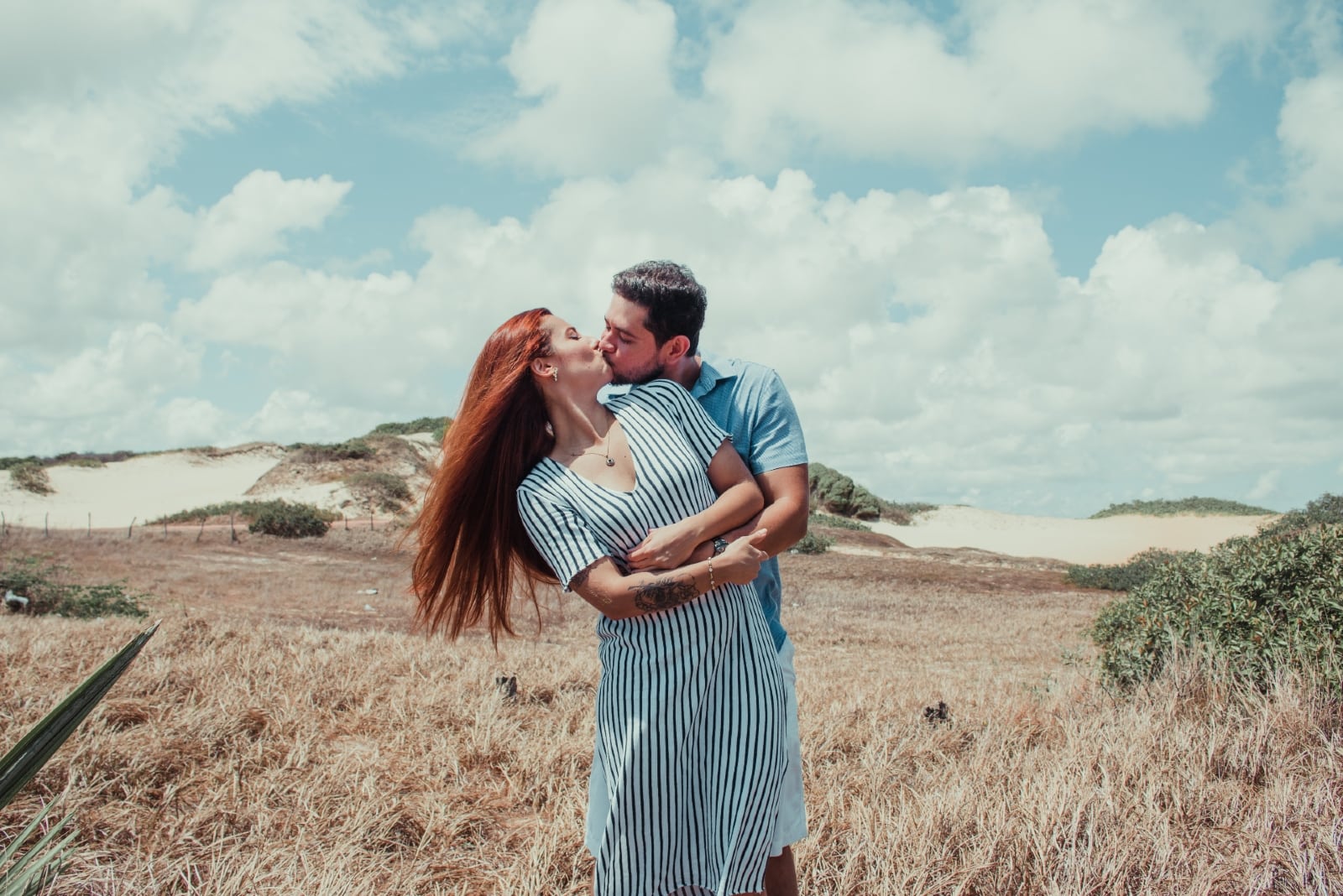 man and woman kissing while standing in the field