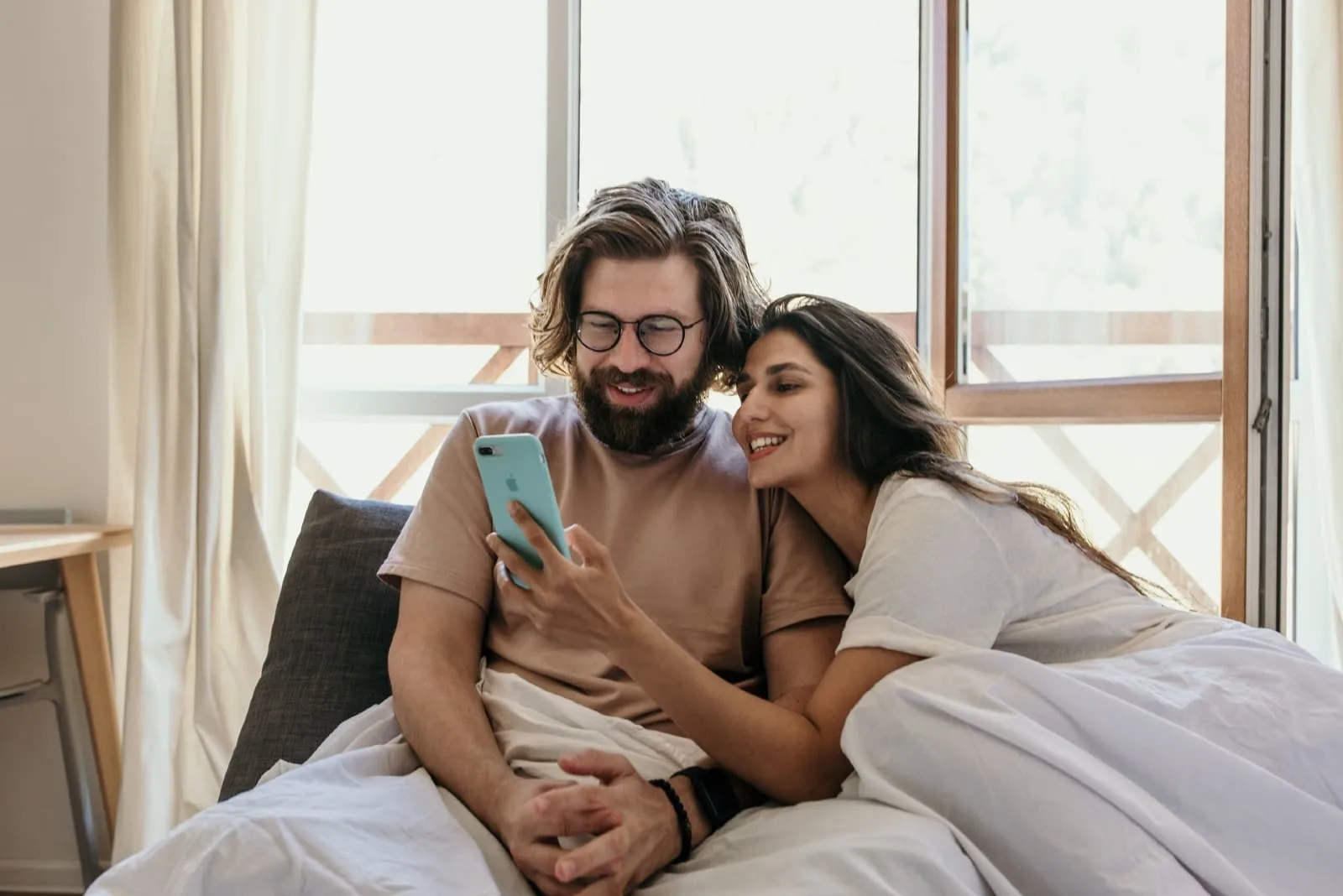 man and woman looking at phone while sitting on bed